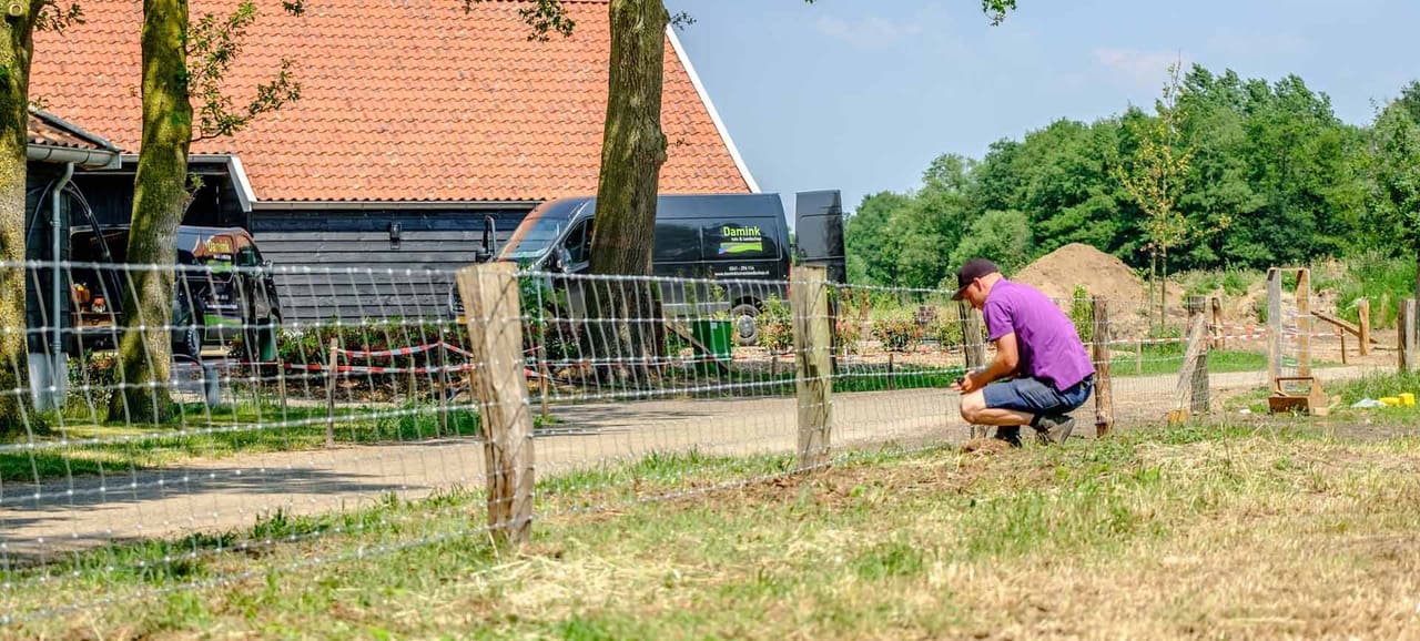 Medewerker van Damink plaatst afrastering langs een weiland, met de bedrijfsbus erachter