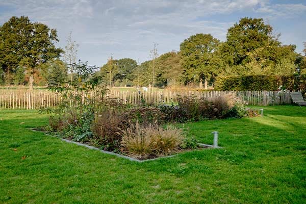 Plantvak in het gazon, met een kastanjehouten hek naar het landschap
