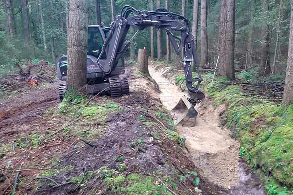 Graafmachine werkt aan een watergang in het naaldbos